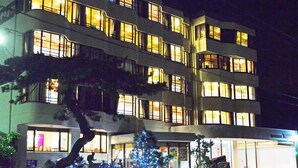 Un hôtel à plusieurs étages, avec des fenêtres illuminées et un sapin de Noël en premier plan.