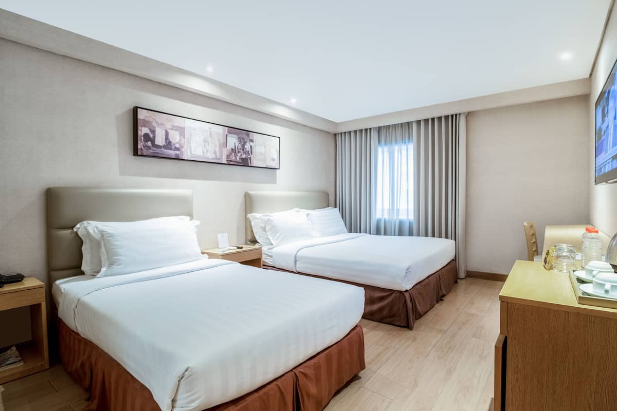 Une chambre d’hôtel avec deux lits, un bureau, une chaise, une table de chevet et un tableau au mur.