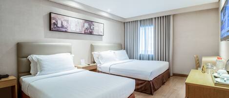 A hotel room with two beds, a desk, a chair, a nightstand, and a painting on the wall.