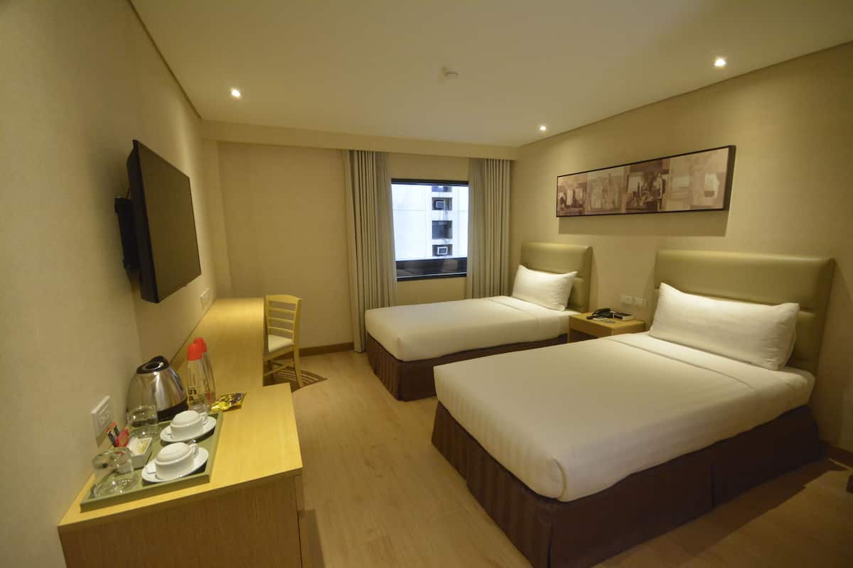 Une chambre d’hôtel avec deux lits, un bureau avec une chaise, un téléviseur à écran plat, une fenêtre avec des rideaux et un tableau au mur.