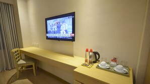A hotel room with a TV mounted on the wall displaying a news program, a wooden desk with a chair, and a tray with cups and a kettle. - Jinjiang Inn Ortigas (Pasig)