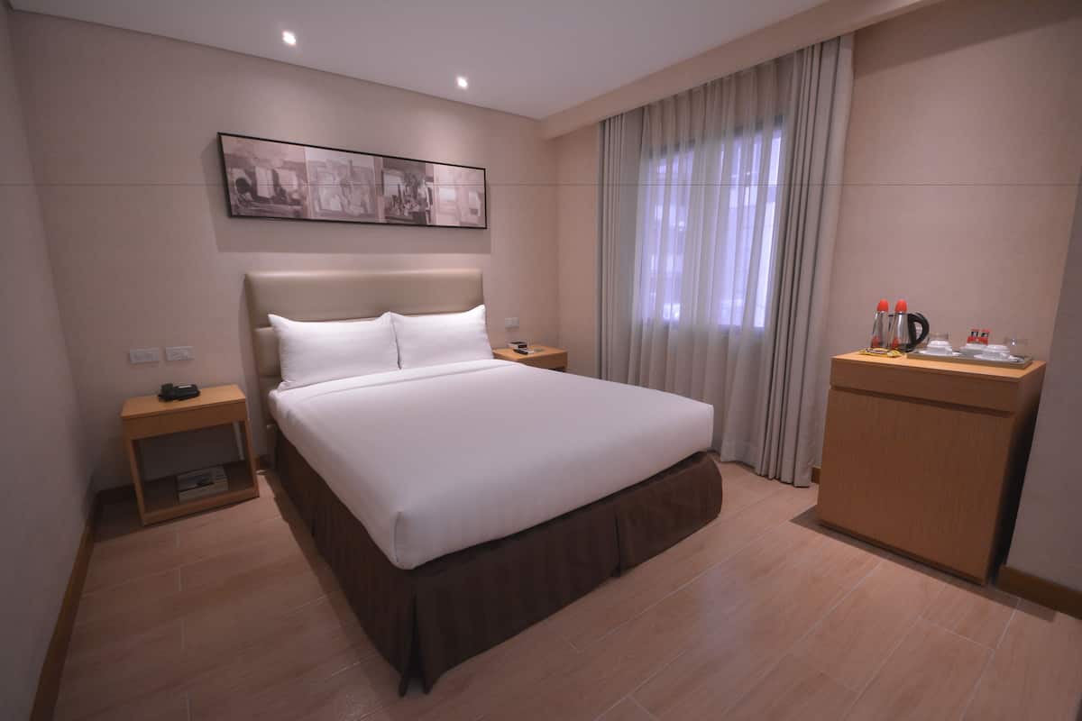 Une chambre d’hôtel avec un grand lit, une table de chevet, un bureau avec une chaise et une fenêtre avec des rideaux.