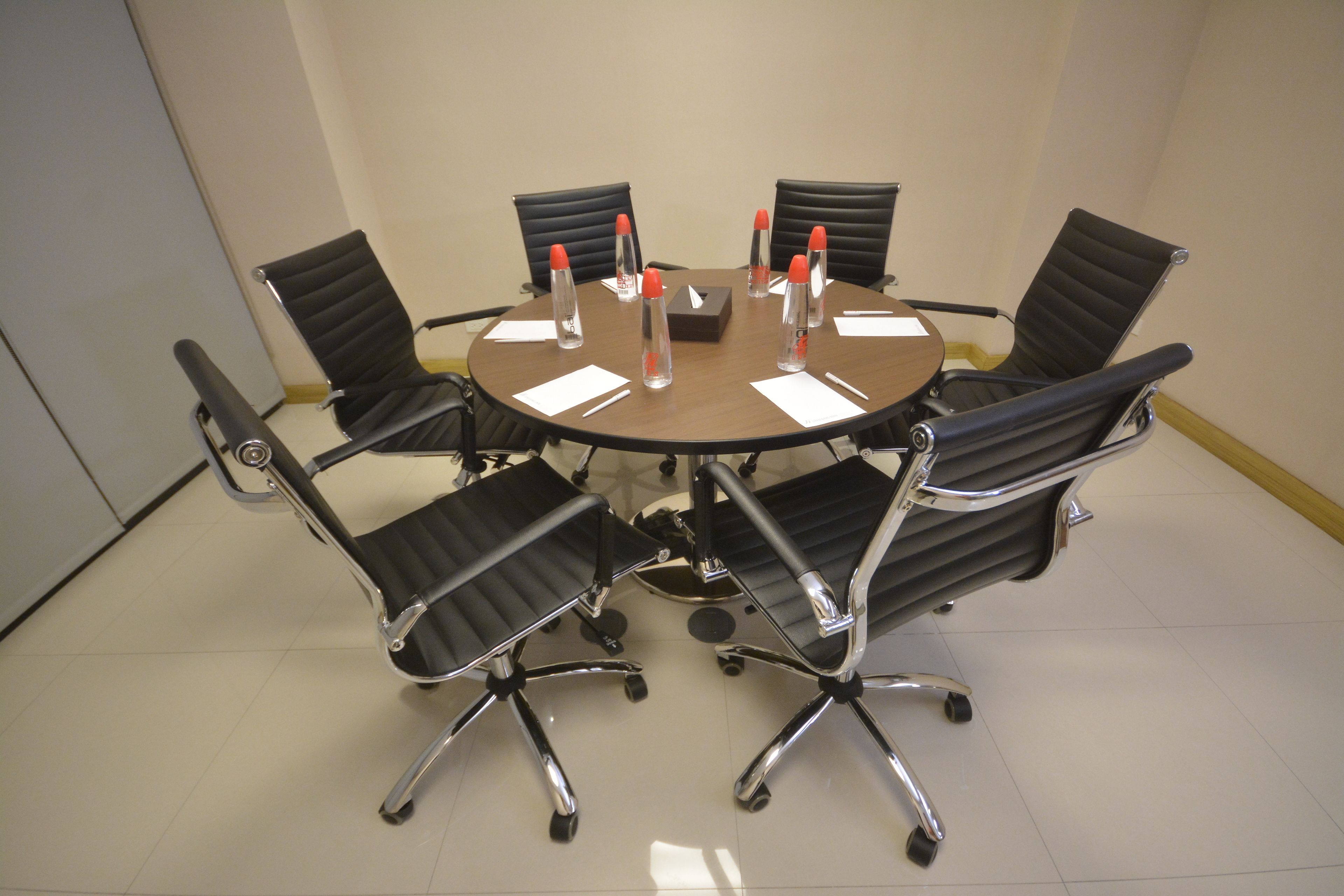 A conference room with a round table, six black office chairs, and water bottles on the table.