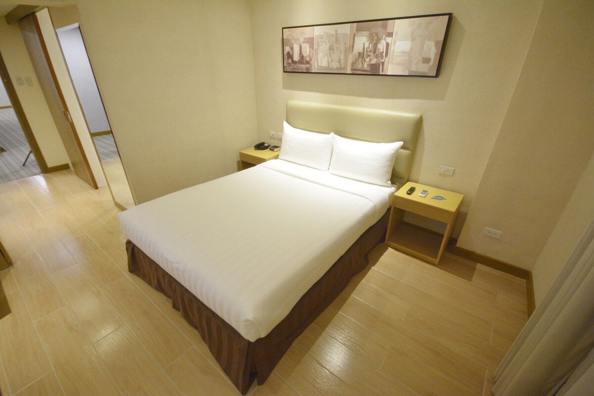 A hotel room with a large bed, a headboard, two bedside tables, and a wall-mounted artwork.