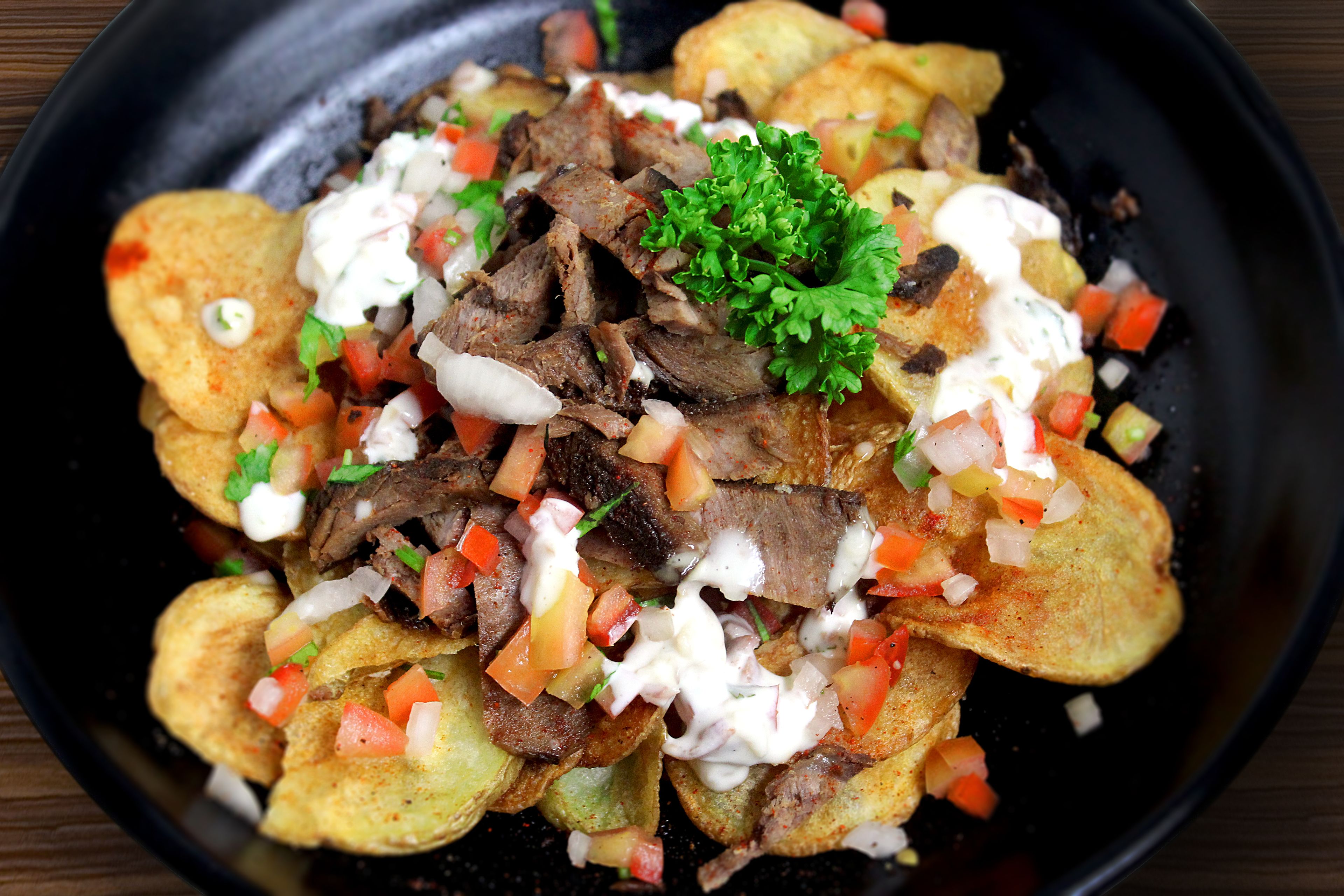 A bowl of nachos topped with meat, diced tomatoes, onions, and a garnish of parsley.
