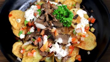 A bowl of nachos topped with meat, diced tomatoes, onions, and a garnish of parsley.