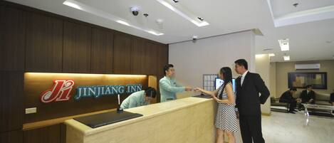 A reception desk with a sign reading "Jinjiang Inn" and a man and woman standing in front of it.