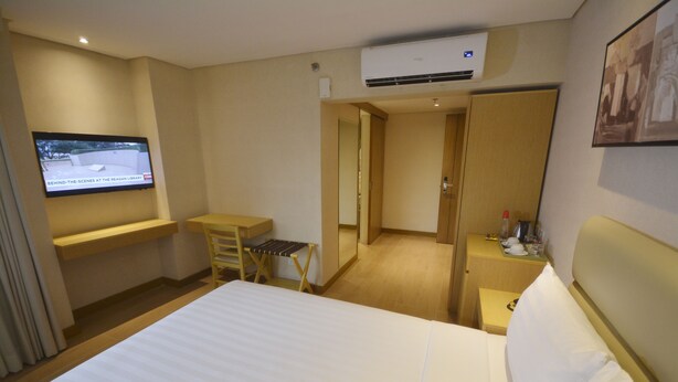 A hotel room with a bed, a desk, a chair, a TV mounted on the wall, and an air conditioning unit. - Jinjiang Inn Ortigas (Pasig)