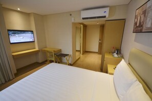 Ein Hotelzimmer mit Bett, Schreibtisch, Stuhl, einem an der Wand befestigten Fernseher und einer Klimaanlage.