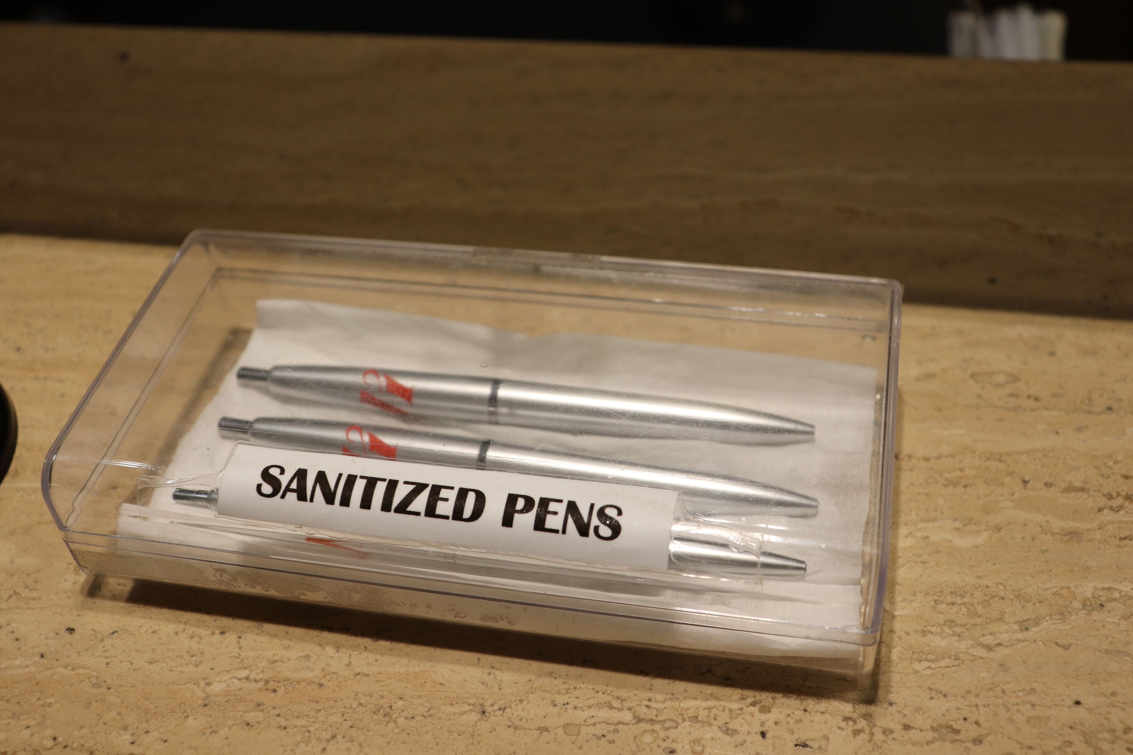 A clear plastic box labeled "SANITIZED PENS" containing several pens.