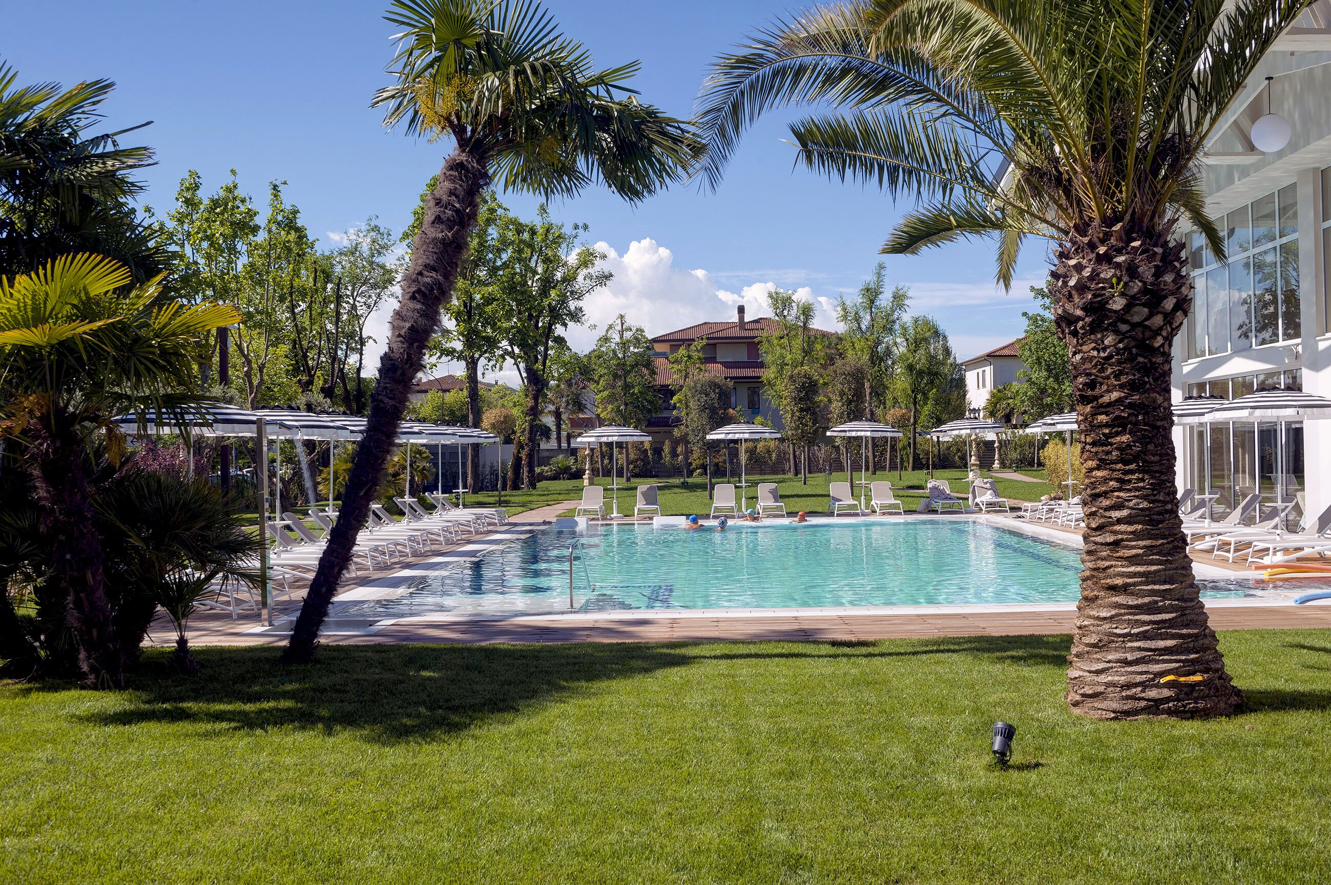 Una piscina circondata da palme e lettini, con un edificio sullo sfondo.