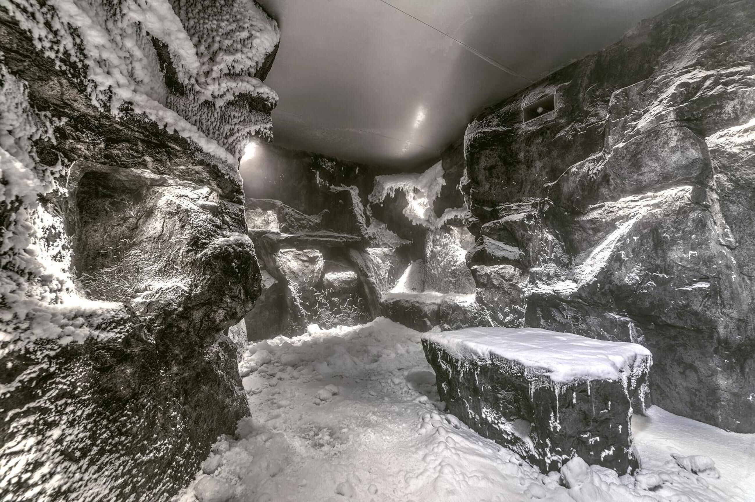 Interno di una grotta innevata, con formazioni rocciose e una panchina.