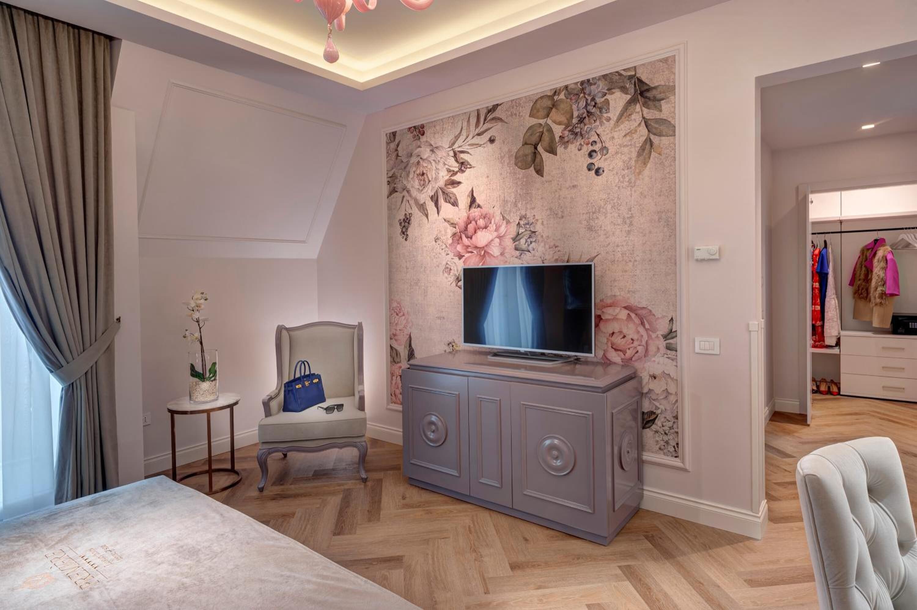 A bedroom with a television on a cabinet, a chair, a small table with a vase, and a wardrobe.