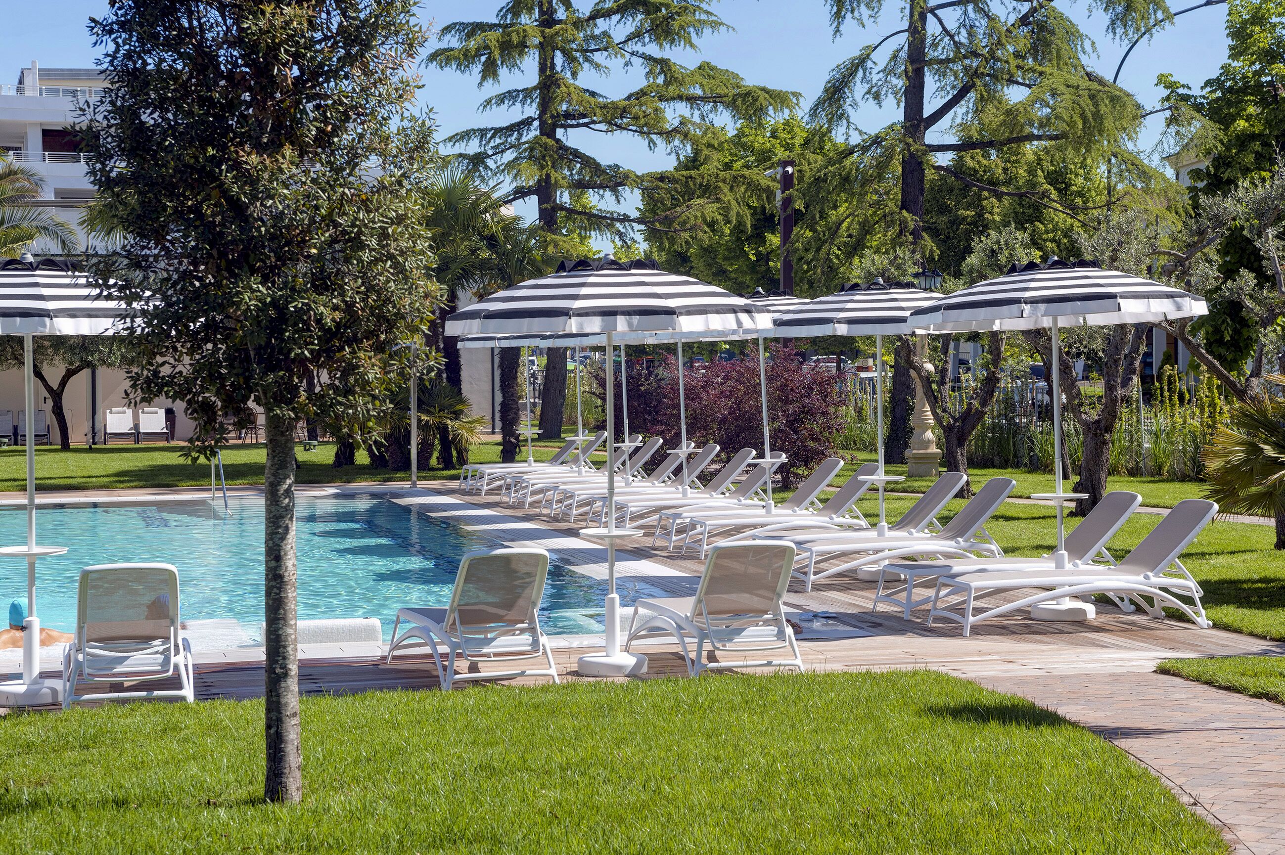 A pool area with lounge chairs and umbrellas, surrounded by greenery and trees.