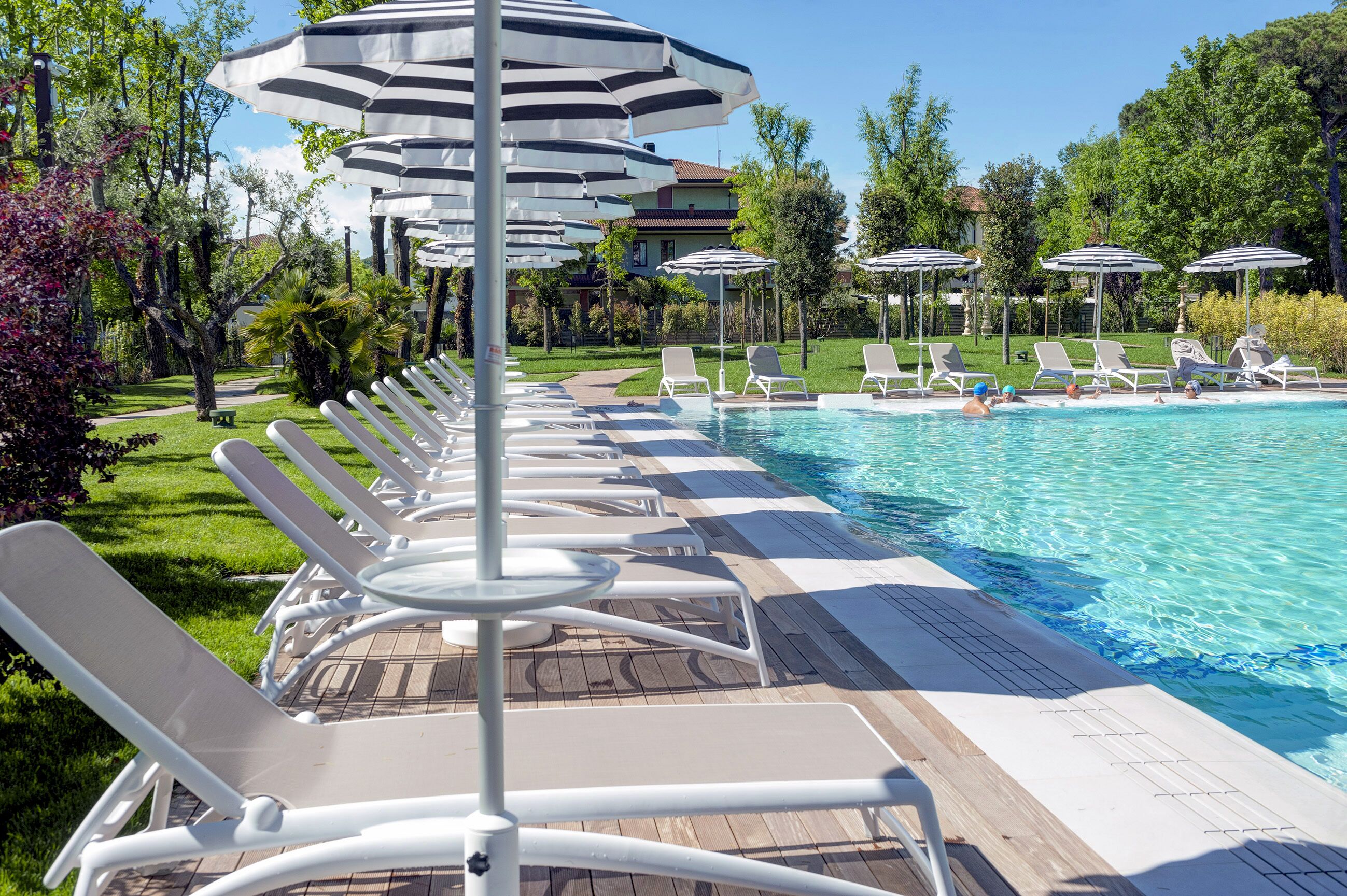 A poolside area with lounge chairs and umbrellas, a clear blue pool, and a landscaped garden.
