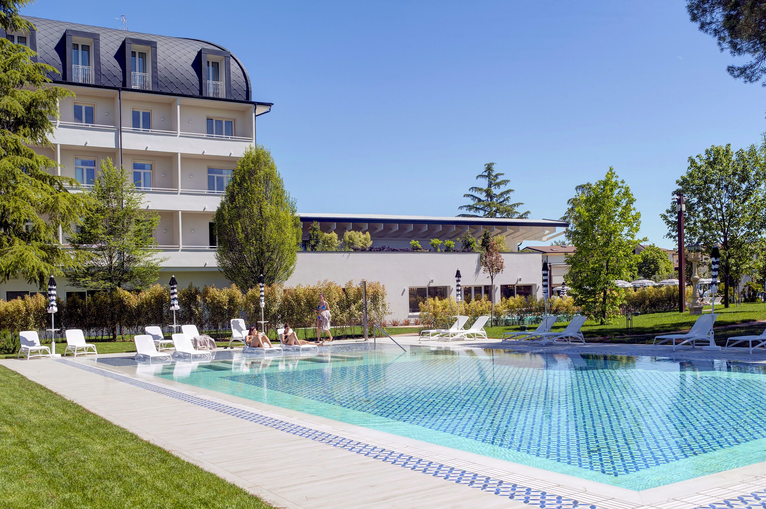 Ein Swimmingpool mit Liegestühlen, ein Gebäude mit Balkonen und ein klarer Himmel.