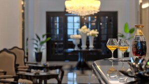 Eine Bar mit zwei Gläsern bernsteinfarbiger Flüssigkeit, einer Flasche roter Flüssigkeit und einer dekorativen Skulptur.