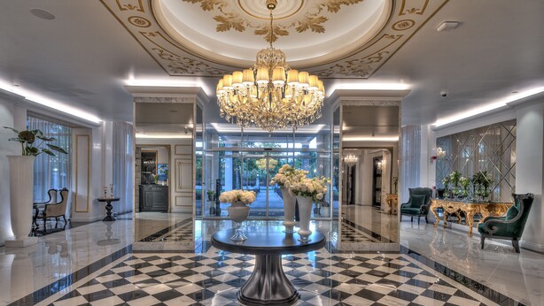 Eine luxuriöse Lobby mit einem Schachbrettmuster-Boden, einem prunkvollen Kronleuchter und edler Ausstattung.