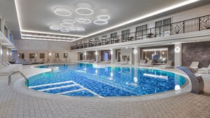 Ein mit modernem Design gestalteter Innenpool, inklusive einer eingelassenen Sitzecke und einem Balkon mit Geländer im zweiten Obergeschoss.