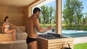 Ein Sauna-Bereich mit Holzbänken, einer Steinliege und Blick auf ein Schwimmbad.