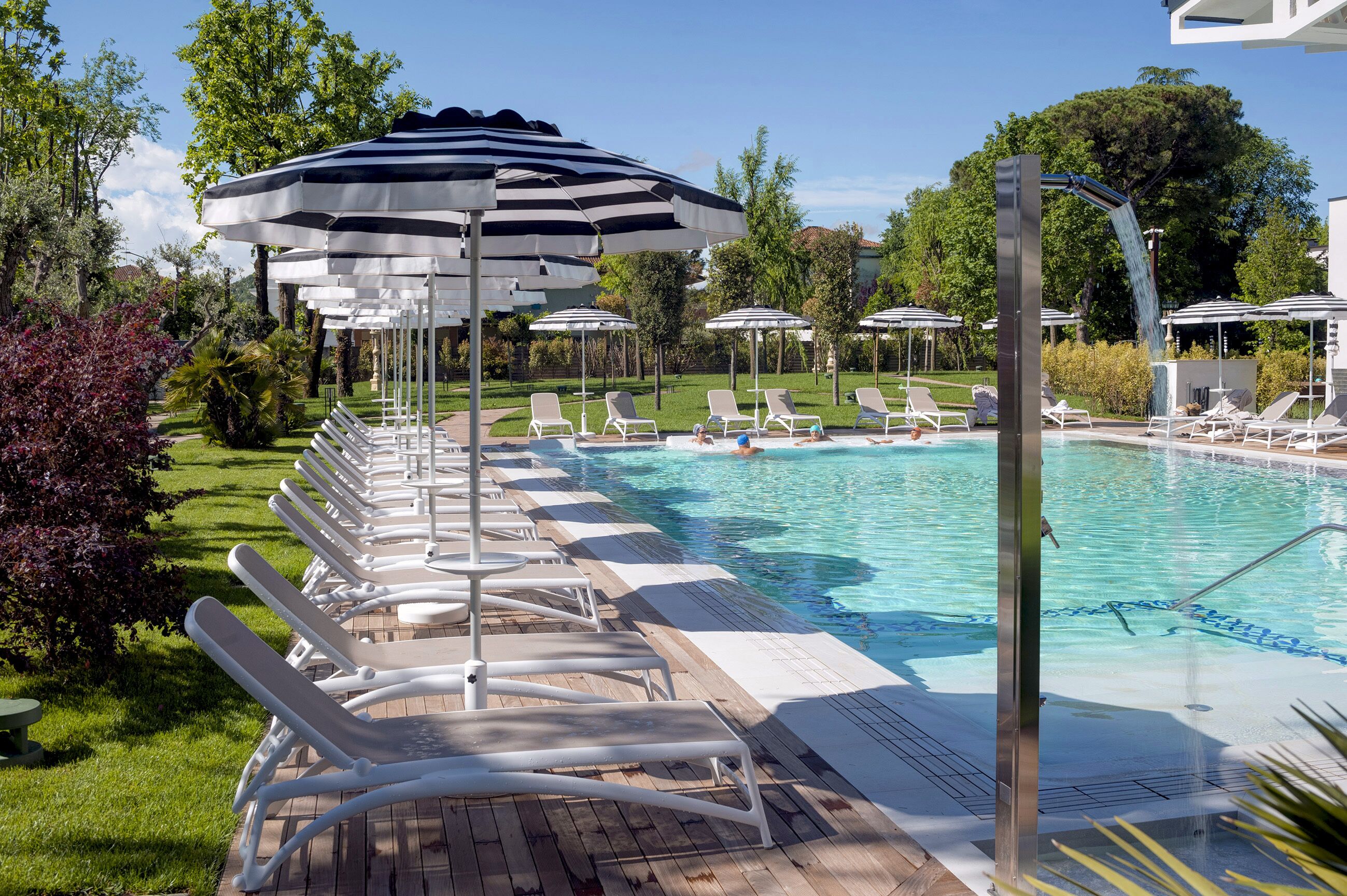 Un espace piscine agrémenté de chaises longues et de parasols, entouré de verdure et d’arbres.