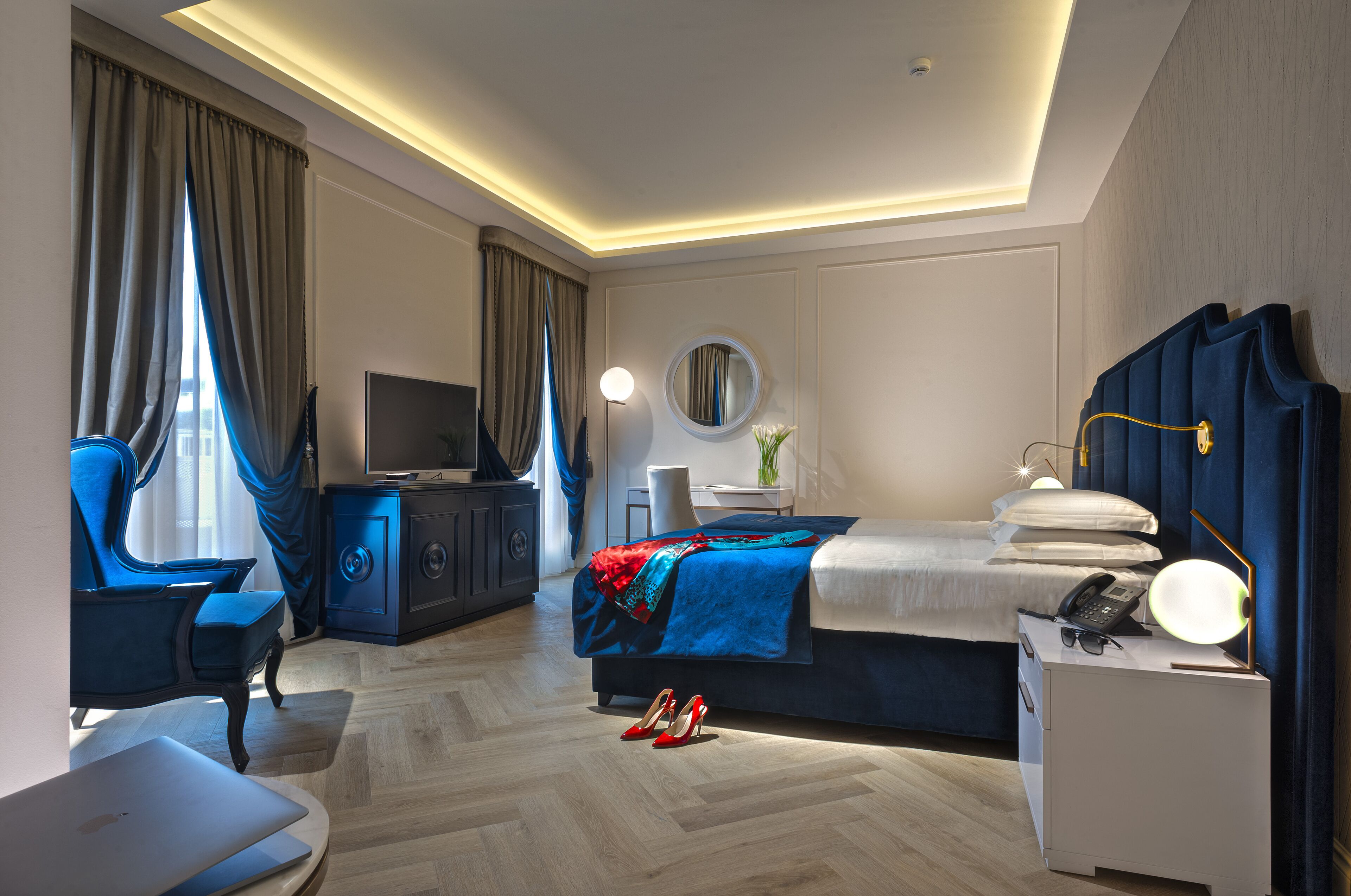 A hotel room with a bed, a desk with a lamp, a chair, a TV, and a wardrobe.