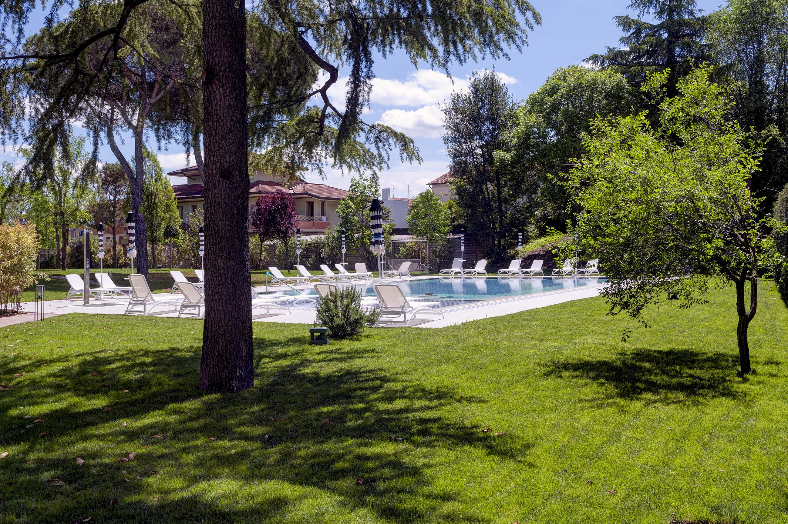 Una piscina con sillas de descanso, rodeada de árboles y un edificio al fondo.