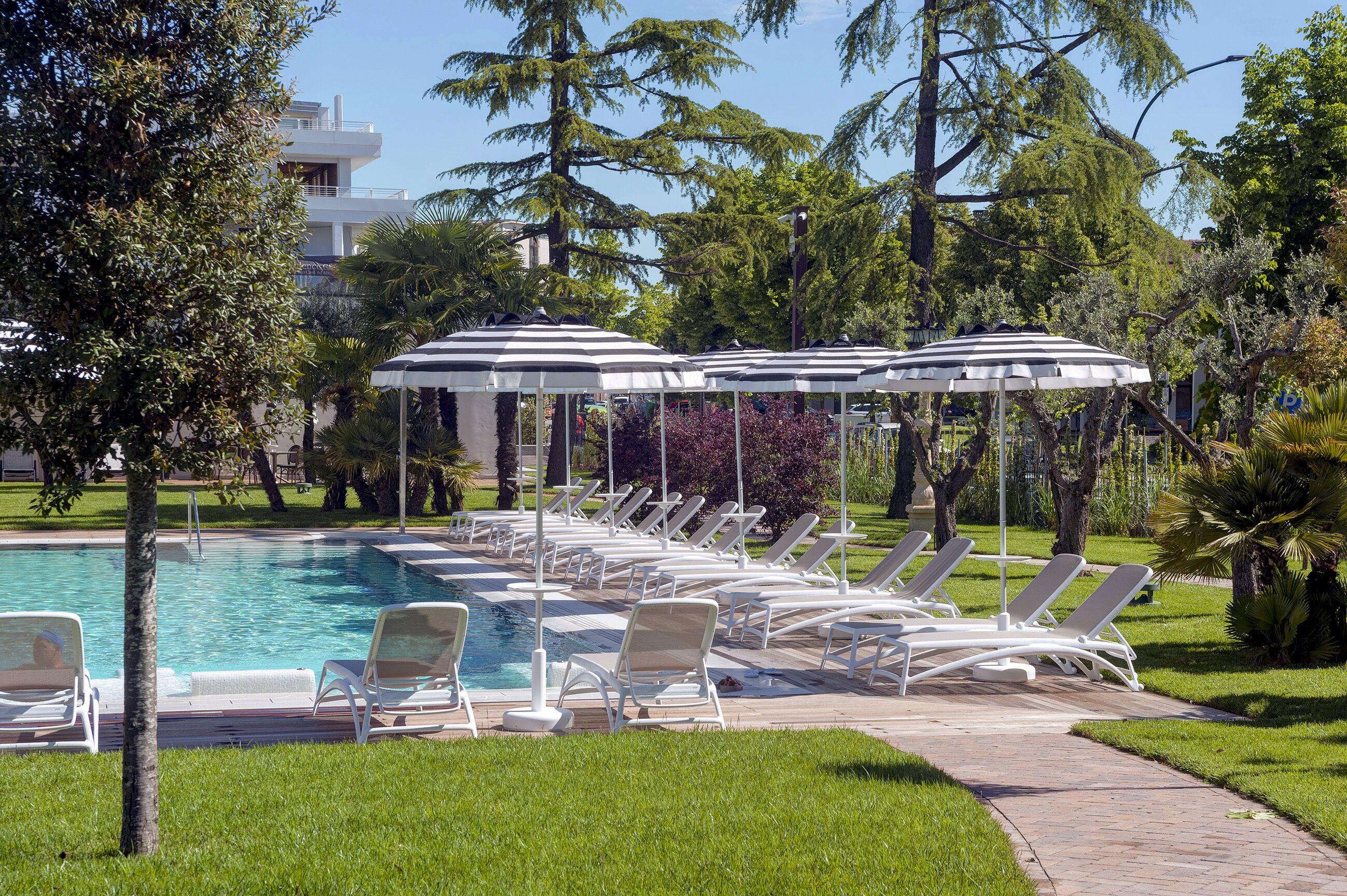 A pool area with lounge chairs and umbrellas, surrounded by trees and a building in the background.