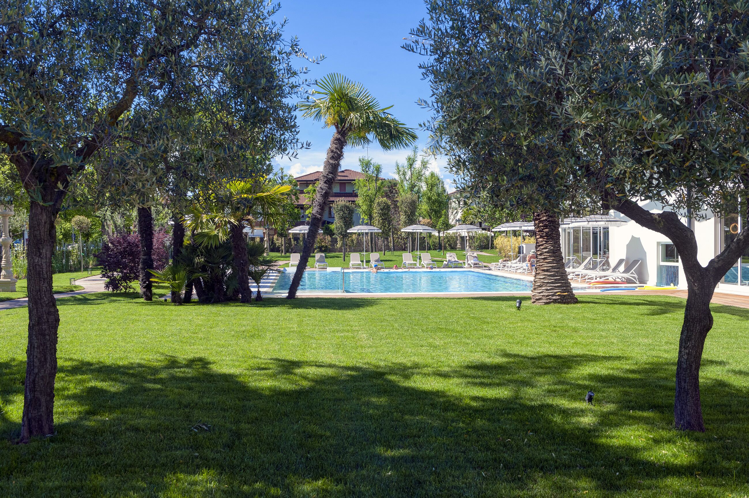 A pool area with lounge chairs and umbrellas, surrounded by trees and a well-maintained lawn.