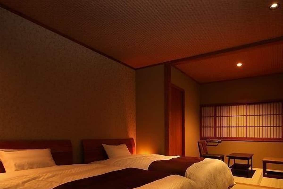 A hotel room with two beds, a window with traditional blinds, and a small table.