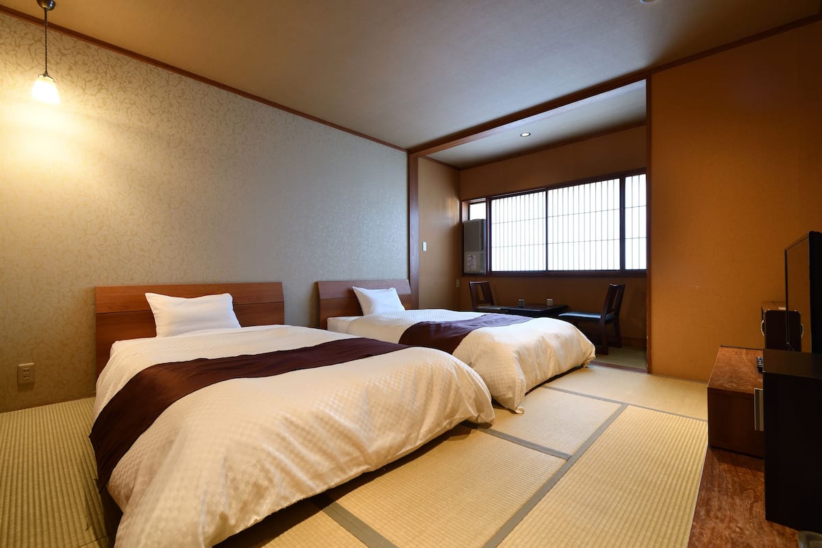 A hotel room with two beds, a wooden headboard, a large window, and a desk with a chair.