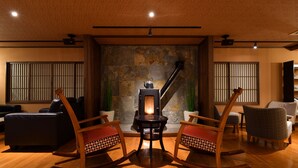 A cozy living room with a fireplace, wooden rocking chairs, and a sofa. - Kusatsu Onsen Ryokan Yoshinoya (Kusatsu)