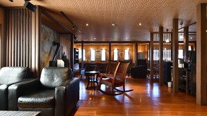 A spacious lounge with leather sofas, a wooden rocking chair, and a polished wooden floor. - Kusatsu Onsen Ryokan Yoshinoya (Kusatsu)