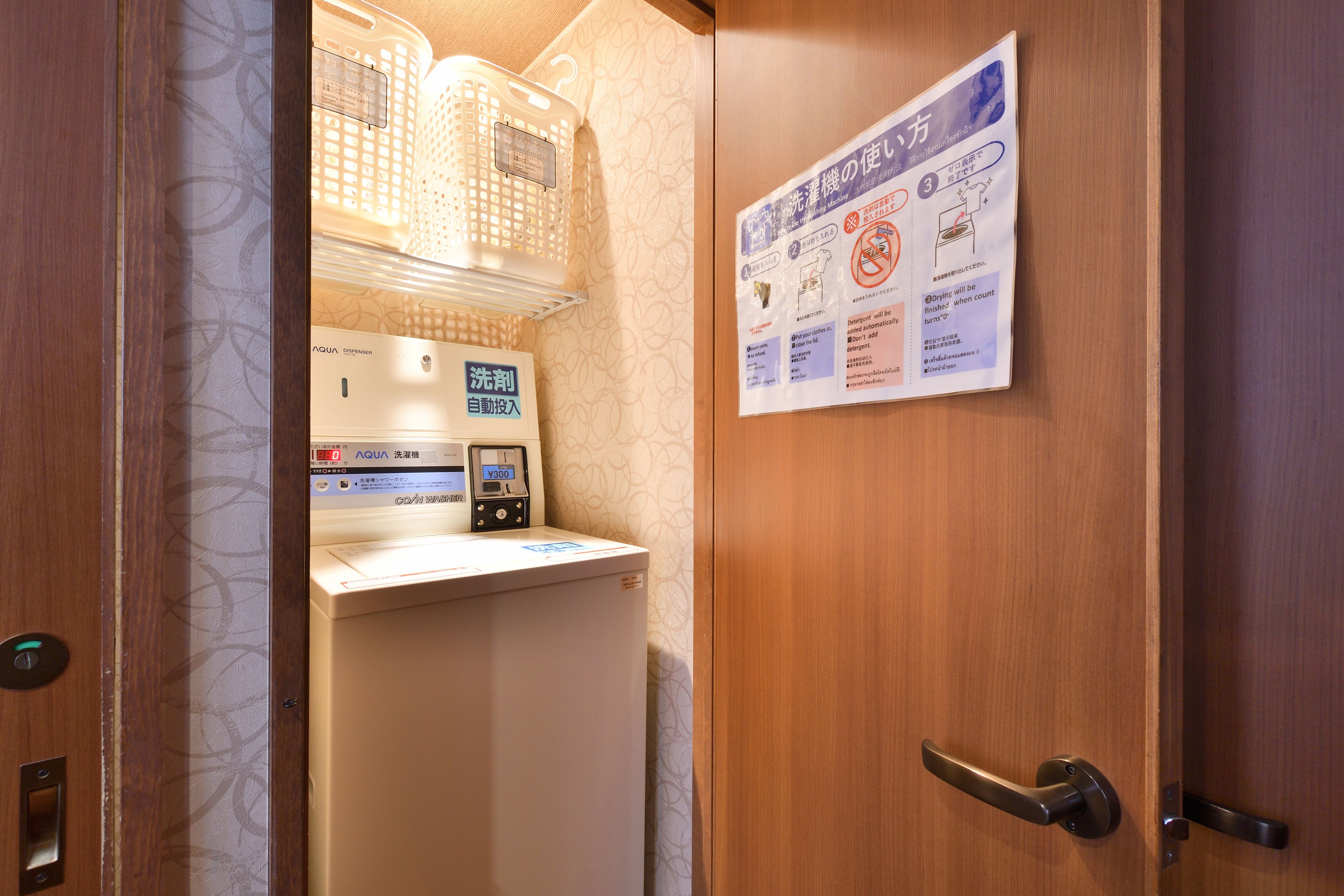 A hotel room with a wooden door, a white washing machine, and a sign with instructions in Japanese.