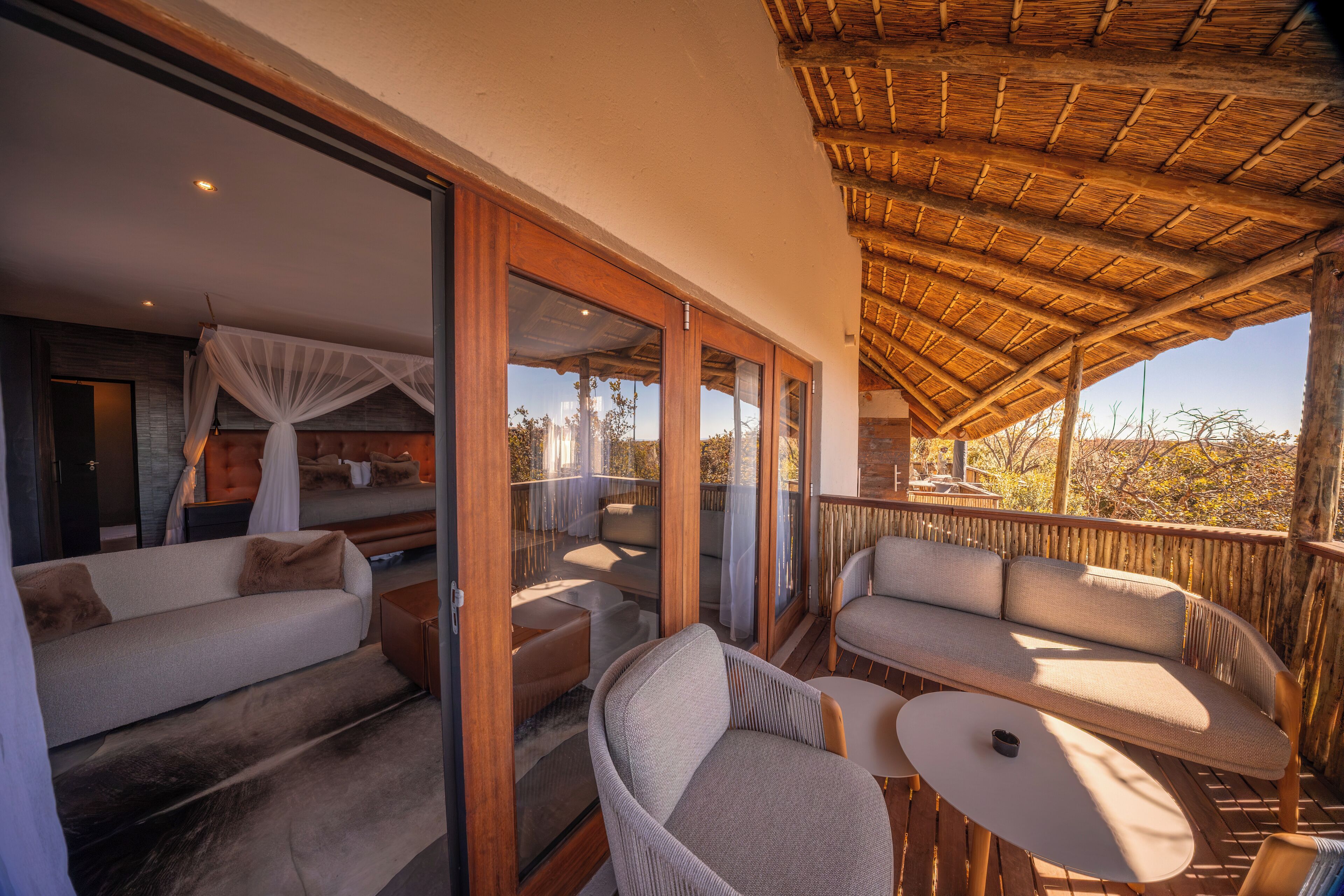 A balcony with a wooden ceiling and glass doors leading to a bedroom with a sofa and a bed.