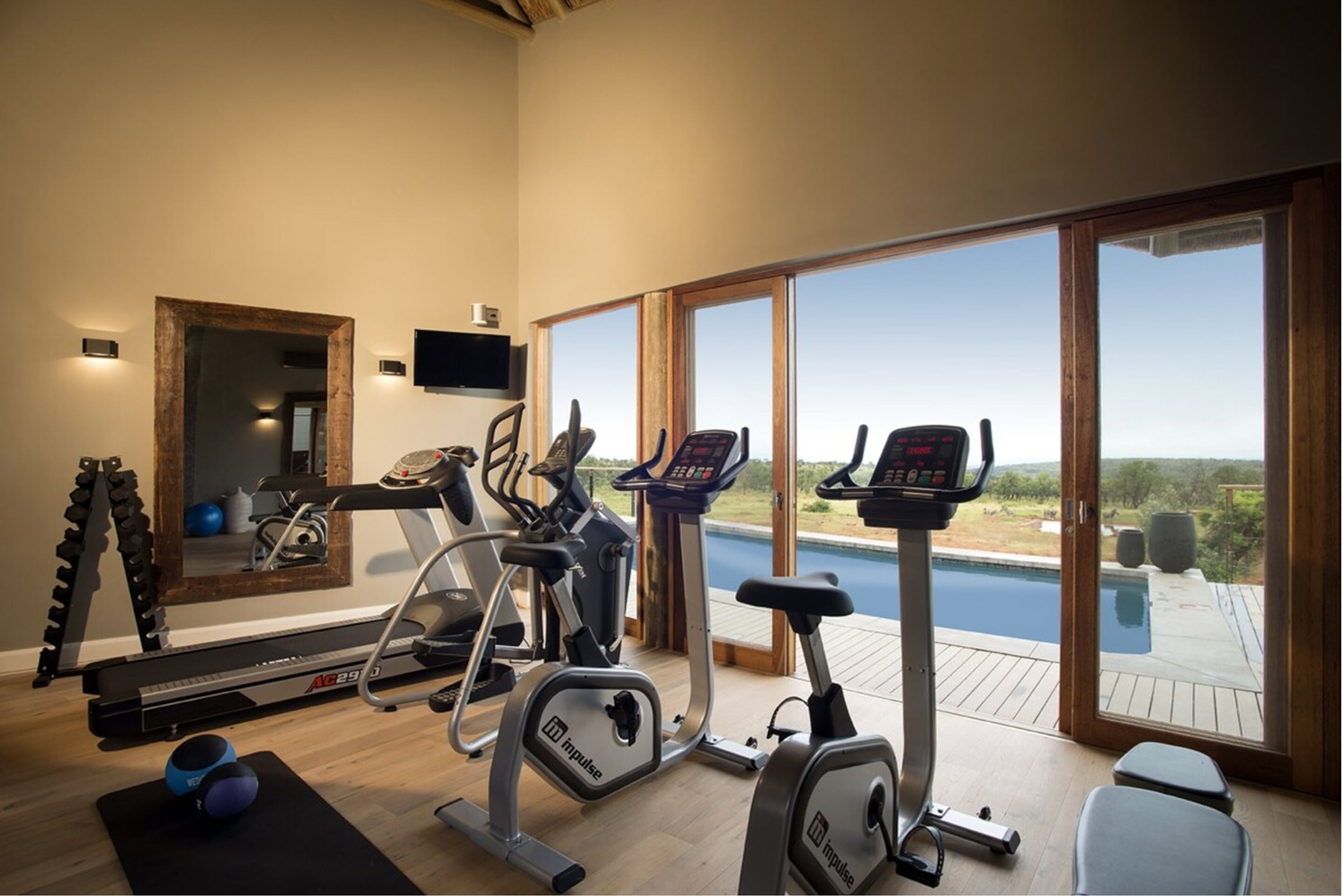 A home gym with exercise equipment, a large mirror, and a view of a swimming pool.