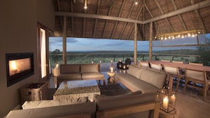 A spacious living area with a large sofa, a TV, and a view of the countryside. - Mhondoro Safari Lodge & Villa (Vaalwater)