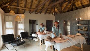 A spa room with three massage tables, wooden benches, and a thatched ceiling.