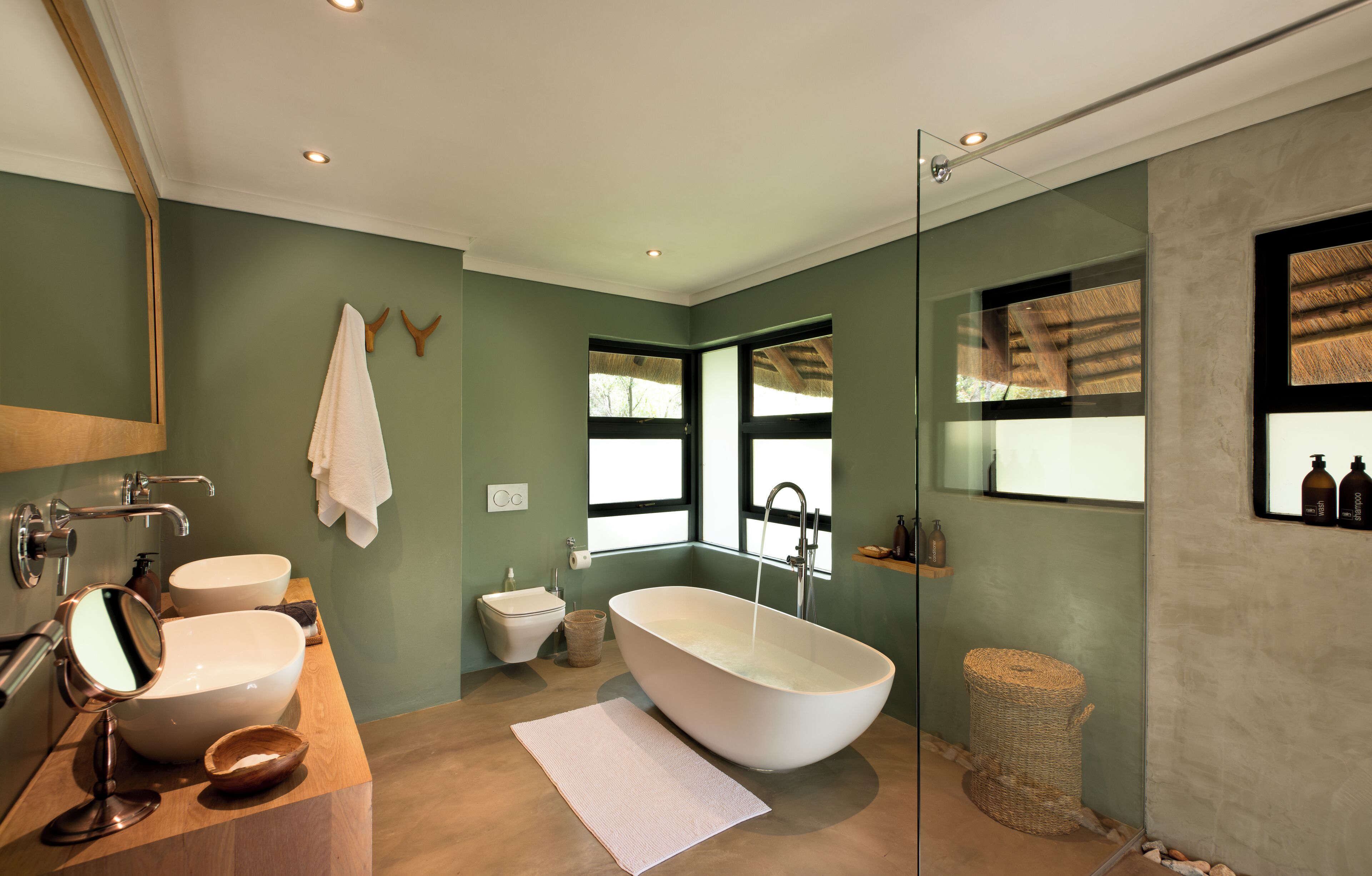 A modern bathroom with a freestanding bathtub, two sinks, a toilet, and a large window providing natural light.