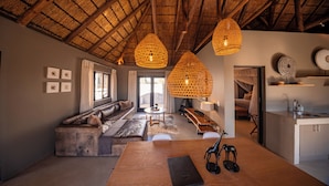 A spacious living area with a high thatched ceiling, a sofa set, a dining table, and a kitchen area. - Mhondoro Safari Lodge & Villa (Vaalwater)