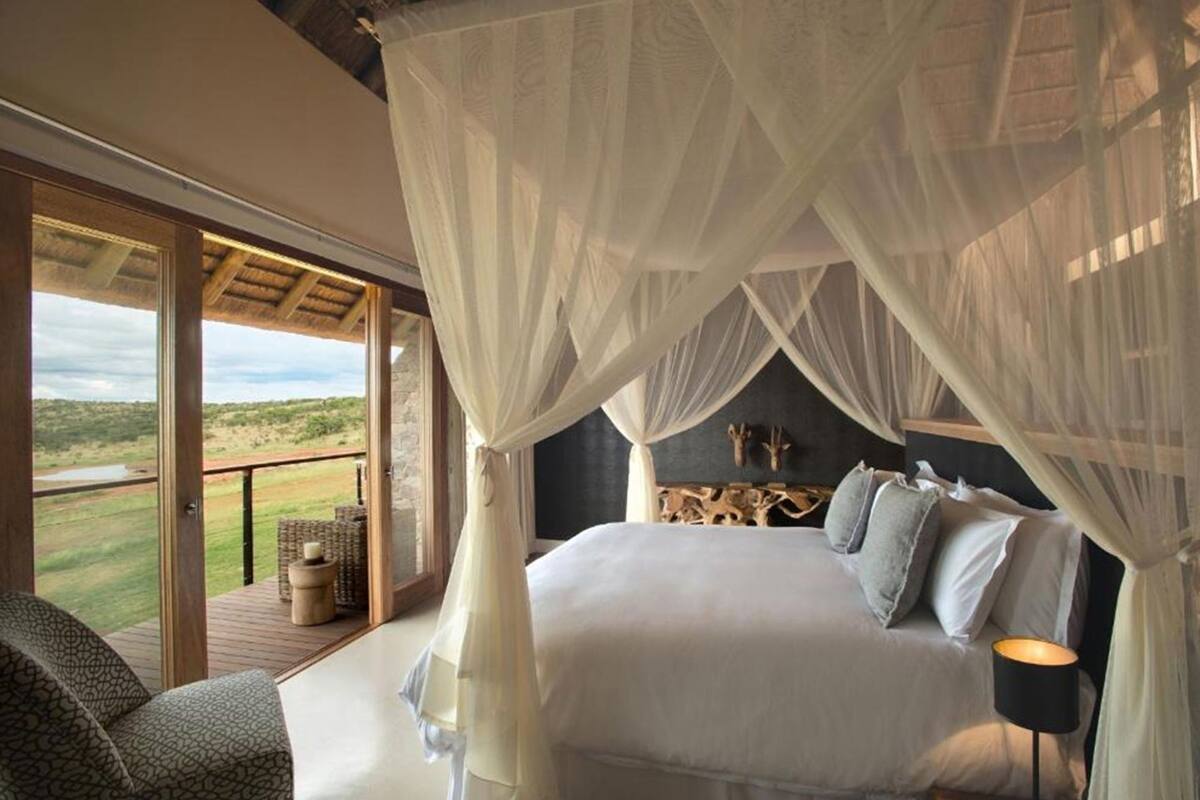 A bedroom with a canopy bed, a view of the outdoors, and a wooden headboard.