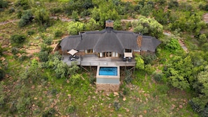An aerial view of a house with a thatched roof, a swimming pool, and a deck with lounge chairs. - Mhondoro Safari Lodge & Villa (Vaalwater)