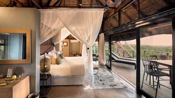 A bedroom with a canopy bed, a desk with a lamp, and a view of the outdoors. - Mhondoro Safari Lodge & Villa (Vaalwater)