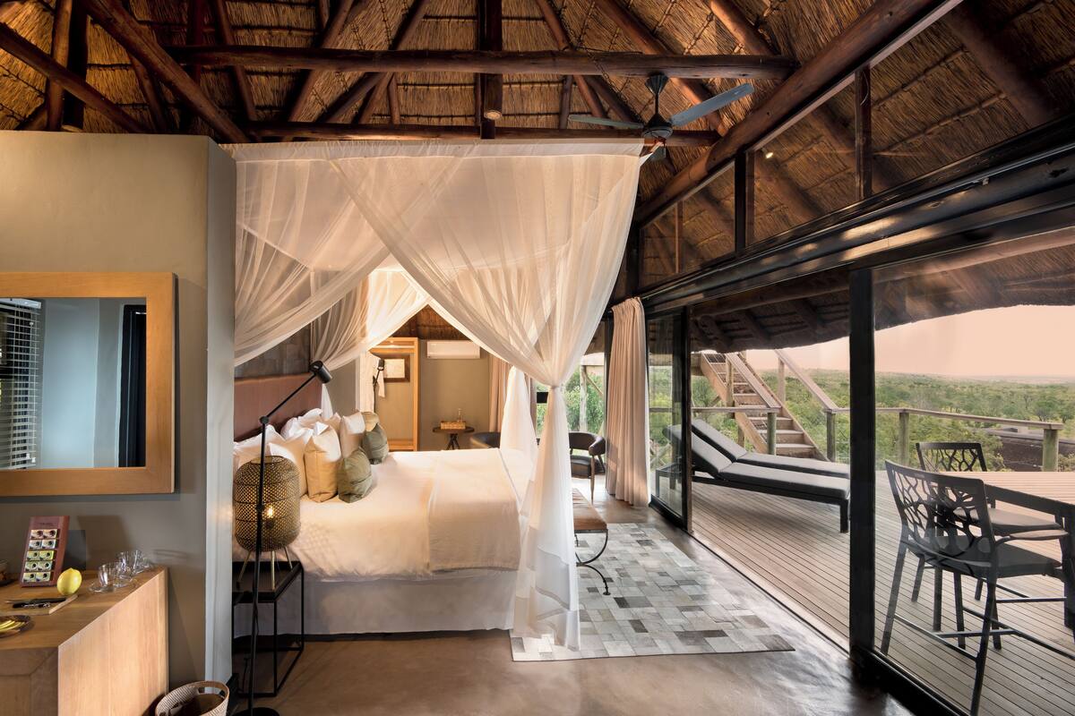 A bedroom with a canopy bed, a desk with a lamp, and a view of the outdoors.