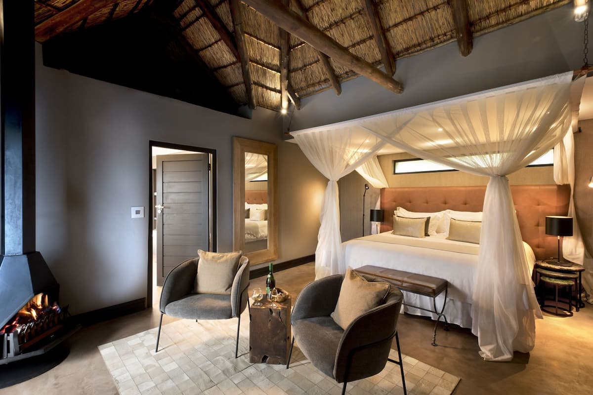 A bedroom with a canopy bed, a fireplace, and a seating area with chairs.