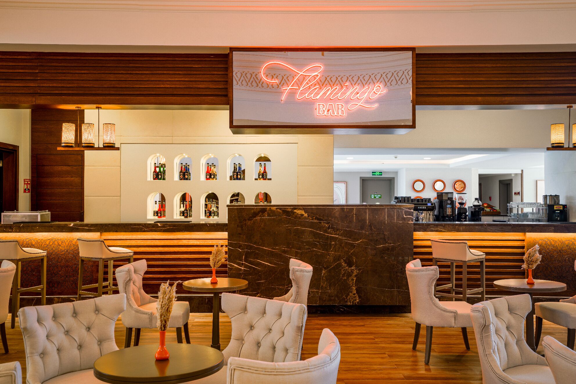 A bar area with a neon sign, seating, and a display of bottles.