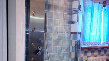 A glass-enclosed shower with a tiled wall, a towel rack, and a window with curtains.