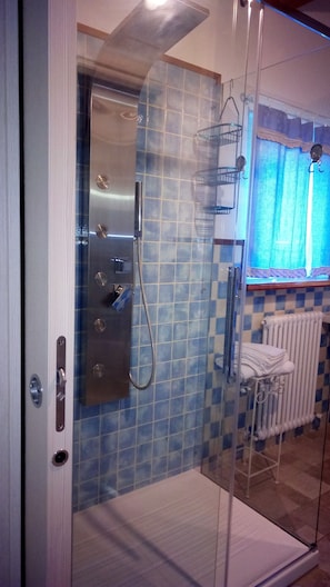 A glass-enclosed shower with a tiled wall, a towel rack, and a window with curtains. - B&B Cadrecca Tra Terra Luna e Mare (Licciana Nardi)