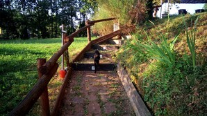Eine Holztreppe führt einen einen grasbewachsenen Hügel hinauf, mit einem Metallgeländer.