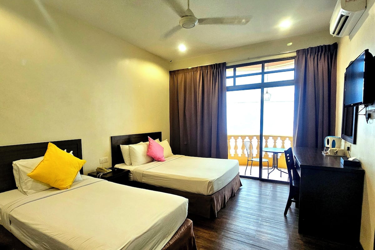 A hotel room with two beds, a desk, a chair, and a balcony with a view.